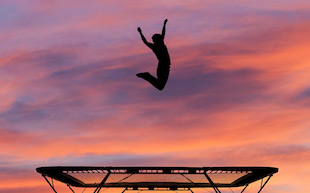 silhouetted man jumping on trampoline in sunset